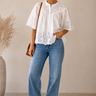 Woman wearing a white blouse with lace details and blue jeans against a beige background