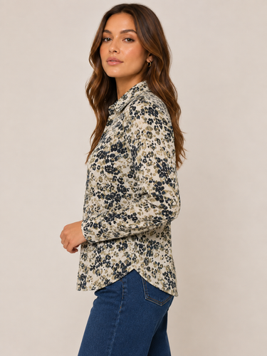 A woman wearing a beige button-up blouse with a navy blue floral pattern, paired with blue jeans, photographed against a solid light beige studio background.
