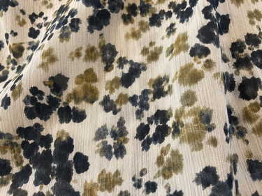 A close-up of a textured fabric with a floral pattern in navy blue and olive green on a warm cream background.