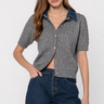 A woman modeling a short-sleeve gray cable-knit cropped cardigan with a contrasting dark blue collar and gold buttons, paired with dark blue jeans against a light gray studio background.