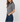 A woman modeling a short-sleeve gray knit button-up shirt with a contrasting dark blue collar, paired with dark blue jeans, against a light gray studio background.