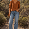 Woman in a desert setting wearing a brown blouse and blue jeans.