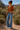 Woman in a rust-colored blouse and blue jeans standing in a desert landscape.