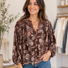 A woman wearing a brown floral long-sleeve blouse with blue jeans, standing in a boutique setting.