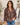 A woman wearing a brown floral long-sleeve blouse with blue jeans, standing in a boutique setting.
