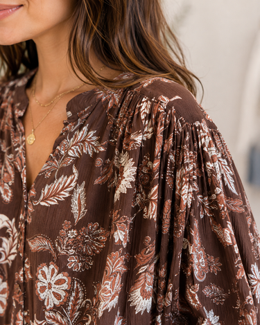 Close-up of a woman wearing a brown bohemian floral print blouse with voluminous sleeves and a V-neckline.