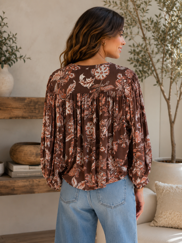 A woman wearing a brown long-sleeve blouse with a floral pattern, shown from the back in a cozy indoor setting.