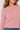 A close-up of a woman wearing a fuzzy, long-sleeve crewneck sweater in a soft dusty pink color, paired with blue jeans.