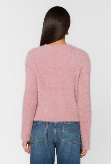 A woman shown from the back wearing a fuzzy, textured light pink long-sleeve sweater and blue jeans against a plain white background.