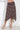 A brown and white polka dot wrap midi skirt worn by a model, shown from the waist down against a white wall.
