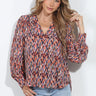 Multicolor abstract print V-neck blouse with long sleeves and button cuffs, styled with light-wash jeans on a model.