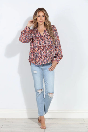 Multicolor abstract print V-neck blouse with long sleeves and button cuffs, styled with light-wash jeans on a model.