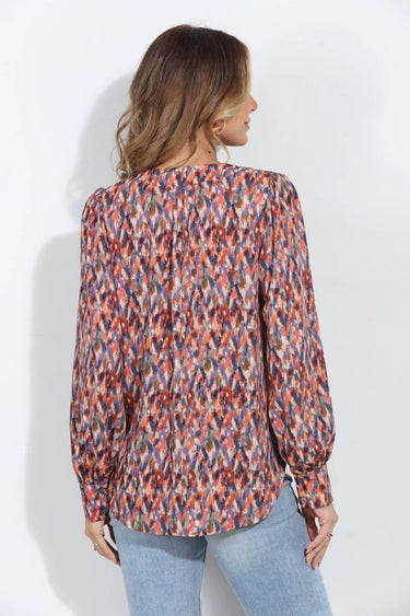 Multicolor abstract print V-neck blouse with long sleeves and button cuffs, styled with light-wash jeans on a model.
