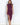 A woman wearing a plum sleeveless ruched midi dress with a draped neckline and thigh-high side slit, styled with neutral heels.