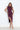 A woman wearing a plum sleeveless ruched midi dress with a draped neckline and thigh-high side slit, styled with neutral heels.