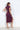 A woman wearing a plum sleeveless ruched midi dress with a draped neckline and thigh-high side slit, styled with neutral heels.