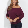 Plum off-the-shoulder three-quarter sleeve top with a relaxed draped fit, styled with dark wash jeans on a model.