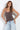 A woman modeling a brown camisole top with white polka dots and light blue jeans against a white studio background.
