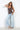 A woman modeling a brown camisole top with white polka dots and light-wash wide-leg jeans against a plain white wall.