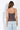 A woman shown from the back wearing a brown camisole top with a white polka dot pattern and light blue jeans, standing against a white wall.