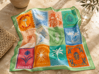 A square patch bandana with a colorful patchwork design featuring palm trees, suns, waves, and tropical motifs, laid out on a beige stone surface with decorative props.
