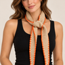 A woman wearing a beige knit scarf with orange stitching on the outside.