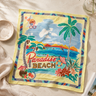 A square beach-themed scarf laid flat on a light beige fabric surface. The scarf features a colorful tropical illustration with palm trees, a blue ocean, mountains, and the words 'Paradise BEACH' in red and gold lettering.