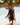 Woman in a black swimsuit standing on a beach with trees and water in the background