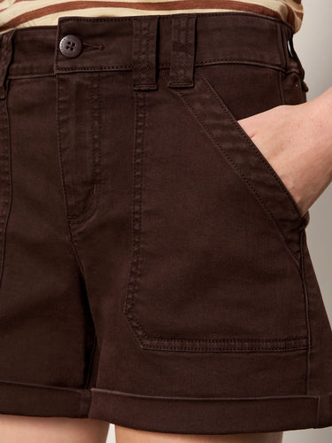 A woman wearing mid rise rich brown shorts on a neutral background