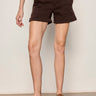 A woman wearing mid rise rich brown shorts on a neutral background