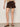 A woman wearing mid rise rich brown shorts on a neutral background