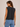 a woman wearing a sleeveless black tank and blue jeans on a neutral background
