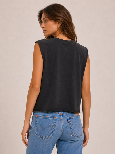 a woman wearing a sleeveless black tank and blue jeans on a neutral background