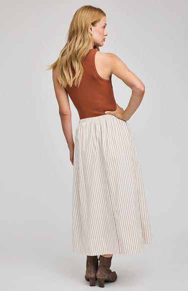Woman wearing a rust-colored top and white pleated skirt on a plain background