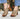 A woman wearing open-toe block-heel sandals with metallic champagne-gold textured uppers, bronze-tone metal studs, and brown wooden soles