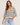 A woman wearing a cream and black horizontally striped knit sweater with elbow-length sleeves and a V-neck, paired with light blue jeans, against a plain light beige background.