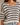 A close-up of a woman wearing a chunky knit sweater with horizontal black and off-white stripes, paired with light blue jeans.