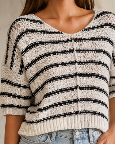 A close-up of a woman wearing a chunky knit sweater with horizontal black and off-white stripes, paired with light blue jeans.