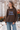Woman wearing a brown knit “Dog Mama” sweater with light blue lettering and relaxed blue jeans in a rustic outdoor setting.