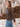 Woman wearing a brown knit “Dog Mama” sweater with light blue lettering and relaxed blue jeans in a rustic outdoor setting.