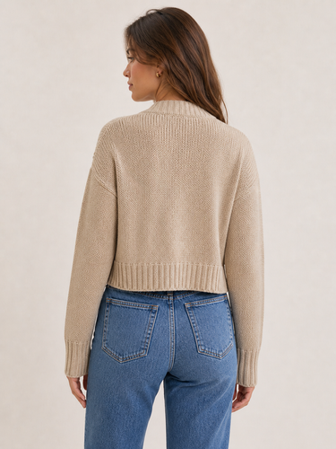 Woman wearing a beige sweater and blue jeans on a plain background