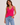 Woman wearing a bright pink ribbed tank top and blue jeans on a plain background