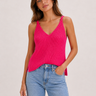 Woman wearing a bright pink ribbed tank top and blue jeans on a plain background
