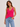 Woman wearing a bright pink ribbed tank top and blue jeans on a plain background