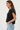A woman shown in side profile wearing a dark charcoal ribbed knit short-sleeve top and light blue jeans against a plain white studio background.