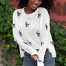 A woman wearing sunglasses and a white distressed skull printed knit sweater.