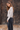 Woman wearing a light oatmeal marled V-neck button-front cardigan with black wide-leg jeans against a rustic wood shingle wall.