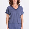 A woman wearing a blue twill v-neck short sleeve top and matching cargo pants on a white background.