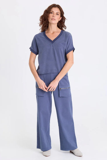 A woman wearing a blue twill v-neck short sleeve top and matching cargo pants on a white background.