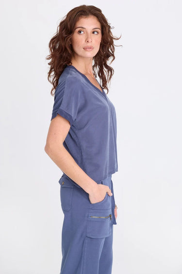 A woman wearing a blue twill v-neck short sleeve top and matching cargo pants on a white background.